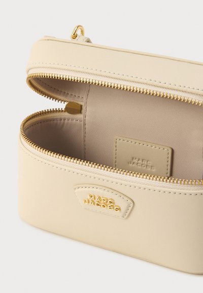 Μπεζ τσαντάκι χειρός από συνθετικό δέρμα με μεταλλικά στοιχεία σε χρυσή απόχρωση, κλείσιμο με φερμουάρ και εσωτερική ετικέτα. Ομαλή υφή, συμπαγής ορθογώνιος σχεδιασμός.