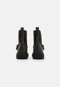 Bottines en cuir marron avec des panneaux élastiques noirs, une fermeture éclair latérale et une semelle en caoutchouc noire. Accents texturés près du haut.