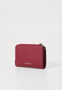Portafoglio in pelle bordeaux con finitura testurizzata, chiusura a zip e accento logo dorato. Forma rettangolare compatta per un facile stoccaggio.