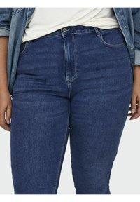 Vaqueros de denim azul oscuro con cintura alta, ligero estiramiento y diseño clásico de cinco bolsillos. Textura suave con un desvanecimiento mínimo y sin adornos.