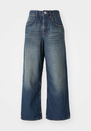 Jeans en denim à jambe large dans un bleu moyen, présentant des poches avant, une fermeture à bouton et à zip, et un léger délavage sur les cuisses.