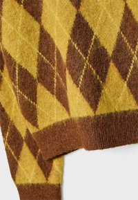 Gros plan sur la manche d'un pull en laine jaune et marron avec un motif losange d'argyle et un poignet côtelé.
