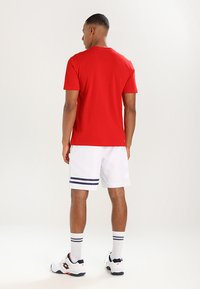 Rød kortermet t-skjorte, hvite idrettsshorts med marineblå striper, hvite sokker og joggesko. Fokuser på design av uformell sportsklær.