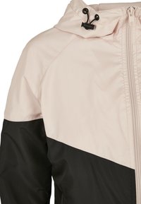 Lätt, vattentålig jacka med övre del i rosa och nedre del i svart, med huva och dragkedja framtill.