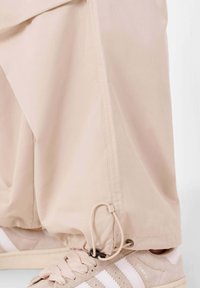 Beige broek van lichtgewicht stof, met een trekkoord aan de zoom en gecombineerd met beige sneakers met witte strepen.