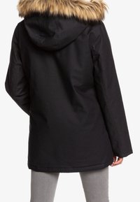 Veste matelassée noire avec capuche bordée de fausse fourrure, manches longues et coupe décontractée, dotée d'un extérieur lisse sans fermetures visibles.