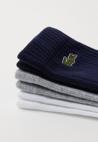 Vier Paare Rippensocken in Marineblau, Grau und Weiß, mit einem gestickten grünen Krokodil-Logo auf dem marineblauen Paar.