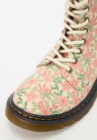 Blomsterpryntet snørebod i pastelfarver, med glat materiale, rund tå, tekstureret stof og en sål med kontrasterende syninger.