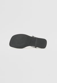 Sole di sandal nero con scanalature testurizzate e area della cinghia ben aderente. Il materiale sembra essere gomma con una finitura liscia, dettagli del marchio minimi visibili.