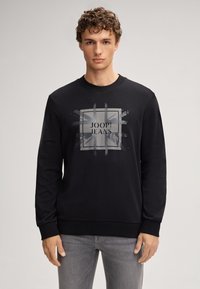 Felpa nera con collo rotondo, maniche lunghe e una grafica frontale grigia con il testo "JOOP! JEANS" all'interno di un design quadrato.