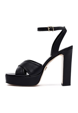 Schwarze Plateau-Sandalette mit hohen Absätzen, gekreuzten Riemen, Knöchelriemen mit Schnalle und dickem Blockabsatz, seitlich auf weißem Hintergrund gesehen.
