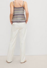 Mönstrad topp med tunnare axelband i flera färger, kombinerad med vita byxor med vida ben. Slätt tyg med avslappnad passform och utan synliga stängningar.