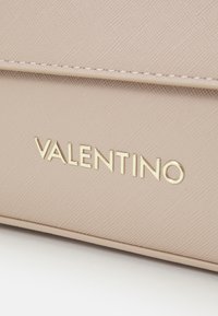 Logo Valentino su materiale beige chiaro strutturato, con finitura liscia e cuciture sottili lungo i bordi.