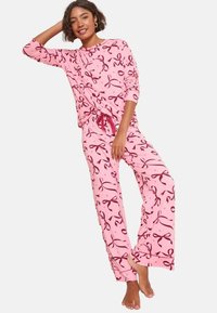 Rosa pyjamaset bestående av en långärmad topp och löst sittande byxor, prydd med kontrasterande bordeauxfärgade snörningsmönster och dragsko i midjan.