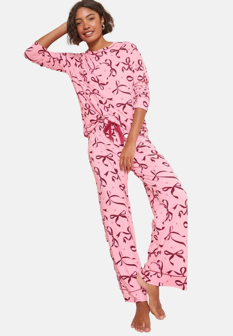 Rosa pyjamaset bestående av en långärmad topp och löst sittande byxor, prydd med kontrasterande bordeauxfärgade snörningsmönster och dragsko i midjan.