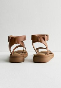 Sandales en cuir marron avec une sangle à boucle, design ouvert, semelle plate et semelle intérieure texturée pour le confort. Fini lisse avec des accents minimalistes.