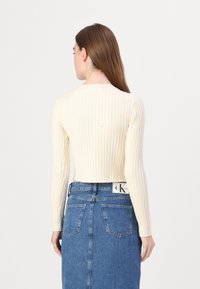 Krémový úpletový top s dlouhým rukávem v jemném ribbed provedení, skvěle doplněný modrou džínovou sukní s vysokým pasem a zadními kapsami. Jednoduchý, strukturovaný design.