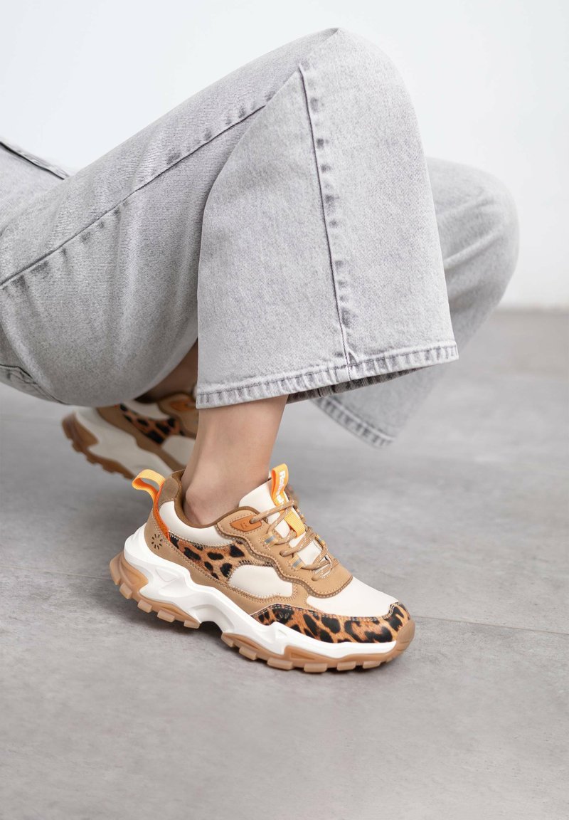 Zapatillas con un diseño en beige y estampado de leopardo, que cuentan con una suela blanca gruesa, acentos naranjas y cordones redondos. Materiales superiores texturizados.