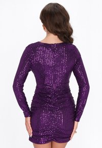 Rochie lungă cu mâneci lungi din paiete mov, cu un design ajustat, având drapaje la talie și un decolteu rotund, evidențiind o textură fină.