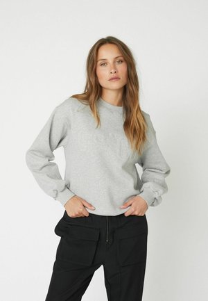 Grauer Baumwoll-Sweatshirt mit geripptem Rundhalsausschnitt und voluminösen Ärmeln, mit geprägtem "Co'Co" Schriftzug auf der Vorderseite. Kombiniert mit schwarzen Cargohosen.