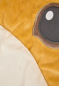 Soft plush surface with yellow and beige colors. Features a large, round eye detail in gray and black fabric, adding a playful design element.