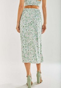 Floral midi skirt in light fabric, featuring a green and pink pattern, with an elastic waistband and a slight sheen. Accompanied by green high heels.