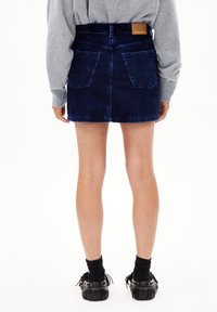 Donkerblauwe corduroy denim minirok met een tailleband, twee achterzakken en een gestikte zoom. Gecombineerd met zwarte schoenen en sokken.