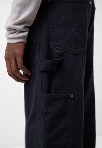 Granatowe spodnie z teksturowanej tkaniny, wyposażone w liczne kieszenie i miedziane wykończenia, o luźnym kroju i prostych nogawkach.