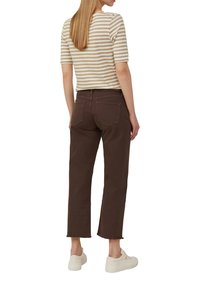Gestreiftes kurzärmliges Oberteil in Beige und Weiß, kombiniert mit braunen, knöchellangen Hosen mit ausgefransten Säumen. Weiße Sneaker runden das Outfit ab.