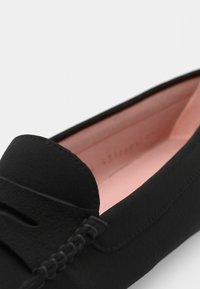 Svart läderloafer med en slät yta, prydd med sömdetaljer och en mjuk rosa inredning. Minimalistisk design med rundad tå.