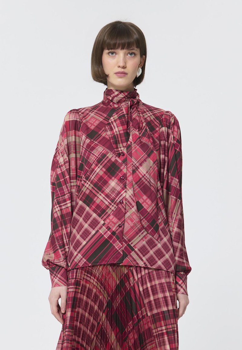 Rode en roze geruite blouse met hoge kraag, lange mouwen en knoopsluiting aan de voorkant; heeft een gladde stof met een gedrapeerde pasvorm en een accent met een lintstrik.