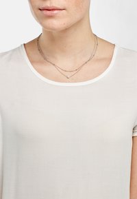 Gelaagde ketting met fijne zilveren kettingen, voorzien van kleine zilveren kralen en een enkele centrale parel, gedragen over een lichte, eenvoudige ronde hals top.