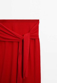 Haut en tissu rouge côtelé avec un détail noué à la taille. Texture douce et couleur unie sans motifs ni embellissements.