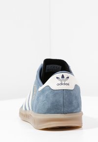 Blue suede sneaker with white stripes, rubber sole, and a white heel tab featuring the Adidas logo. Soft texture with gold accents.