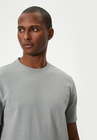 Vaaleanharmaa lyhythihainen t-paita, jossa on ribbikuvio, pyöreä pääntie ja minimalistinen muotoilu. Yksinkertainen ilman kuvioita tai koristeita.