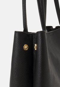 Sac fourre-tout en cuir noir texturé avec deux poignées et des boutons-pression de couleur dorée sur les panneaux latéraux.