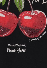 Una tela negra presenta un diseño de dos cerezas rojas con hojas, adornado con detalles brillantes. El texto dice "Mercado de Frutas Nueva York" y "dulce verano".