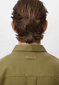 Khaki shirt with a classic collar, smooth texture, and a small rear loop detail, viewed from the back with wavy brown hair visible.