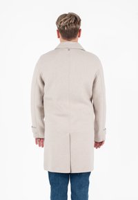 Cappotto in lana beige con taglio dritto, ampio colletto e tasche laterali. Presenta una chiusura con bottoni e una cucitura che corre lungo la schiena.