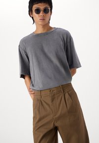 Gray oversized t-shirt with a crew neckline and short sleeves, paired with tan high-waisted pleated trousers. Smooth textures and simple design.