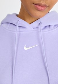 Sweatshirt lilás feito de tecido macio com o logotipo branco da Nike bordado no peito, apresentando um capuz com cordão e punhos canelados.