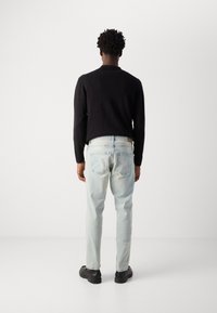 Black long-sleeve top, light blue jeans with a faded finish, and black shoes. The jeans have back pockets and a straight fit design.