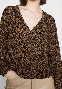 Schwarze Bluse mit tiefem V-Ausschnitt, langen Ärmeln und floralem Muster in Orange- und Brauntönen. Entworfen mit einer lockeren Passform.
