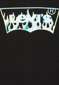 Černé bavlněné tričko s velkým logem Levi's s barevným designem plamenů. Logo má lesklý povrch a je umístěno uprostřed nahoře.