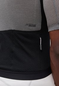 Κοντινή λήψη κοντομάνικου υφασμάτινου ποδηλατικού τζέρσεϊ σε μαύρο και άσπρο χρώμα με μια μικρή τσέπη με φερμουάρ και ορατό φωλίο φερμουάρ.