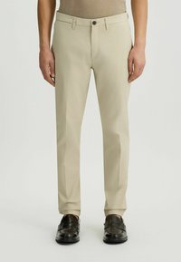 Pantalones beige ajustados con cierre de cremallera y botón. Tejido suave, diseño de pierna recta y bolsillos laterales. 