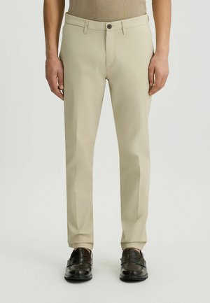 Pantalons beige sur mesure avec fermeture éclair et bouton. Tissu lisse, coupe droite et poches latérales.