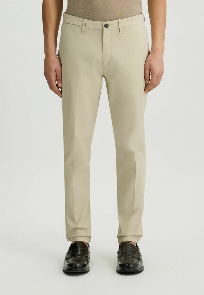 Pantalones beige ajustados con cierre de cremallera y botón. Tejido suave, diseño de pierna recta y bolsillos laterales. 