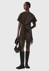 Tmavohnedé olivovo zelené šaty s krúteným detailom v páse, s čipkovým lemom. Skombinované s čiernymi čižmami po kolená a malou čiernou taškou.