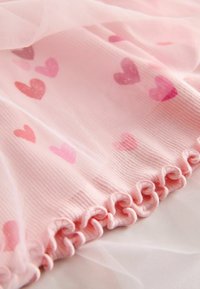 Világos rózsaszín áttetsző anyag, amelyen sötétebb rózsaszín szívek találhatók elosztva, fodros alsó szegéllyel a plusz textúra és részletek érdekében.